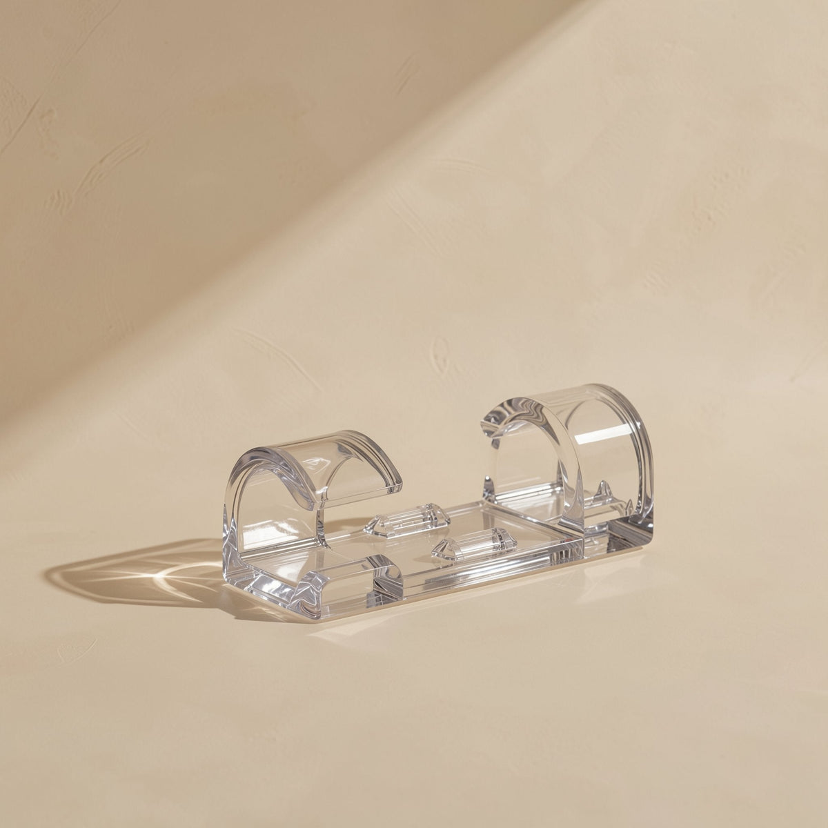 Close-up of a single clear Stickcord self-adhesive cable clip with open buckle arches on a beige surface