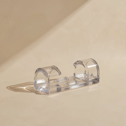 Close-up of a single clear Stickcord self-adhesive cable clip with open buckle arches on a beige surface