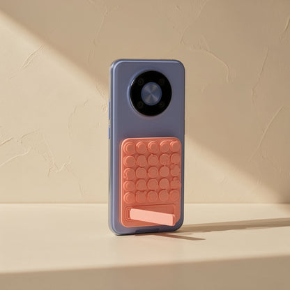 Gripcup – Coral suction cup pad on a blue phone with the kickstand partly extended, standing upright on a ledge