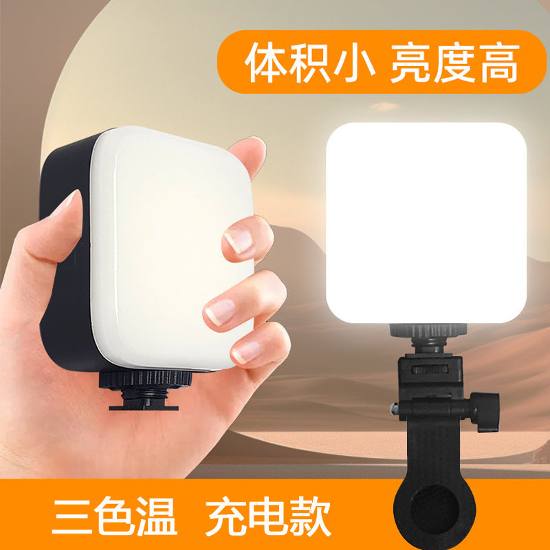 Pocketbeam Handheld Square LED Camera Fill Light held in a hand beside a lit panel on a black clamp mount