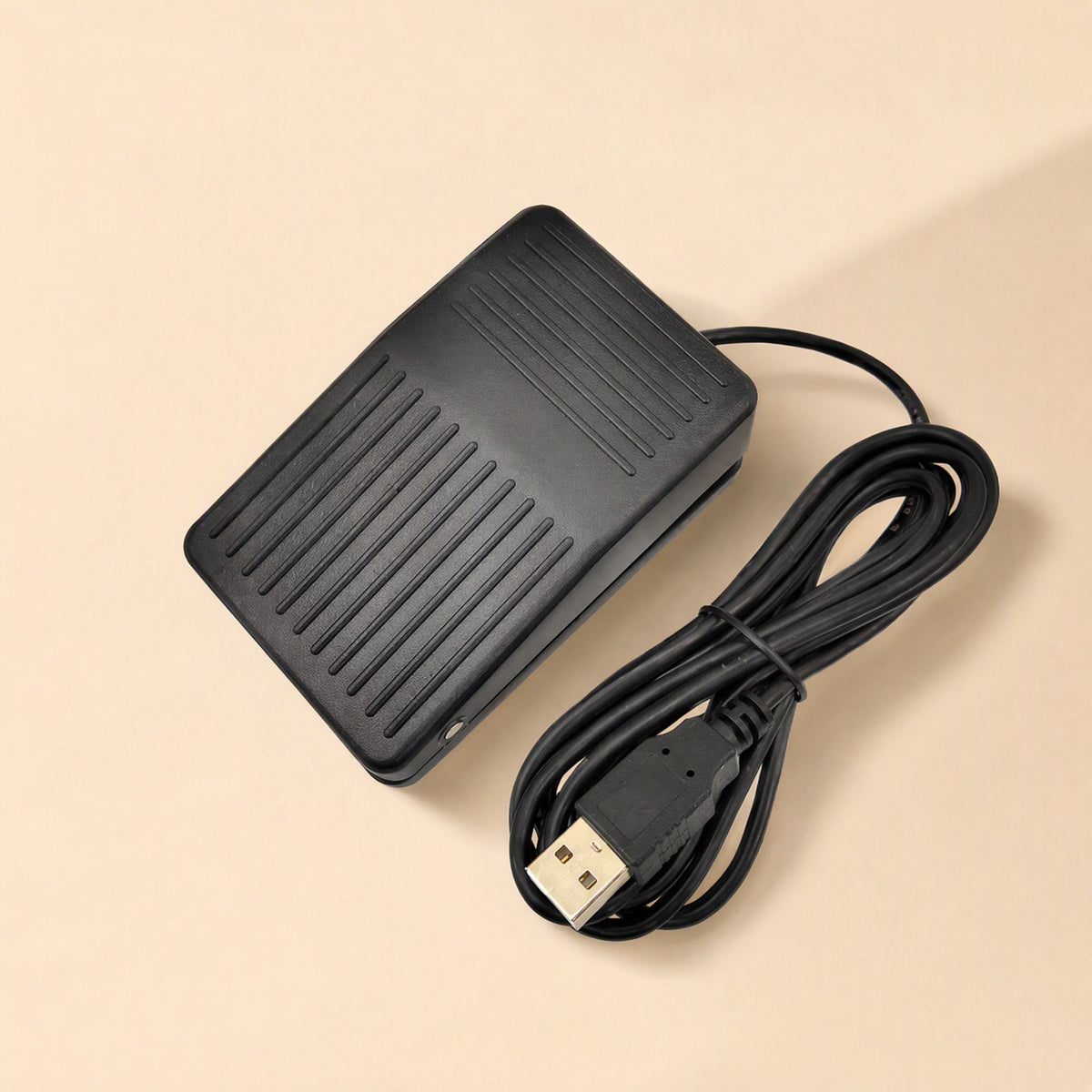 Tapstep USB Foot Pedal Switch in black with coiled USB cable on a beige background, top view