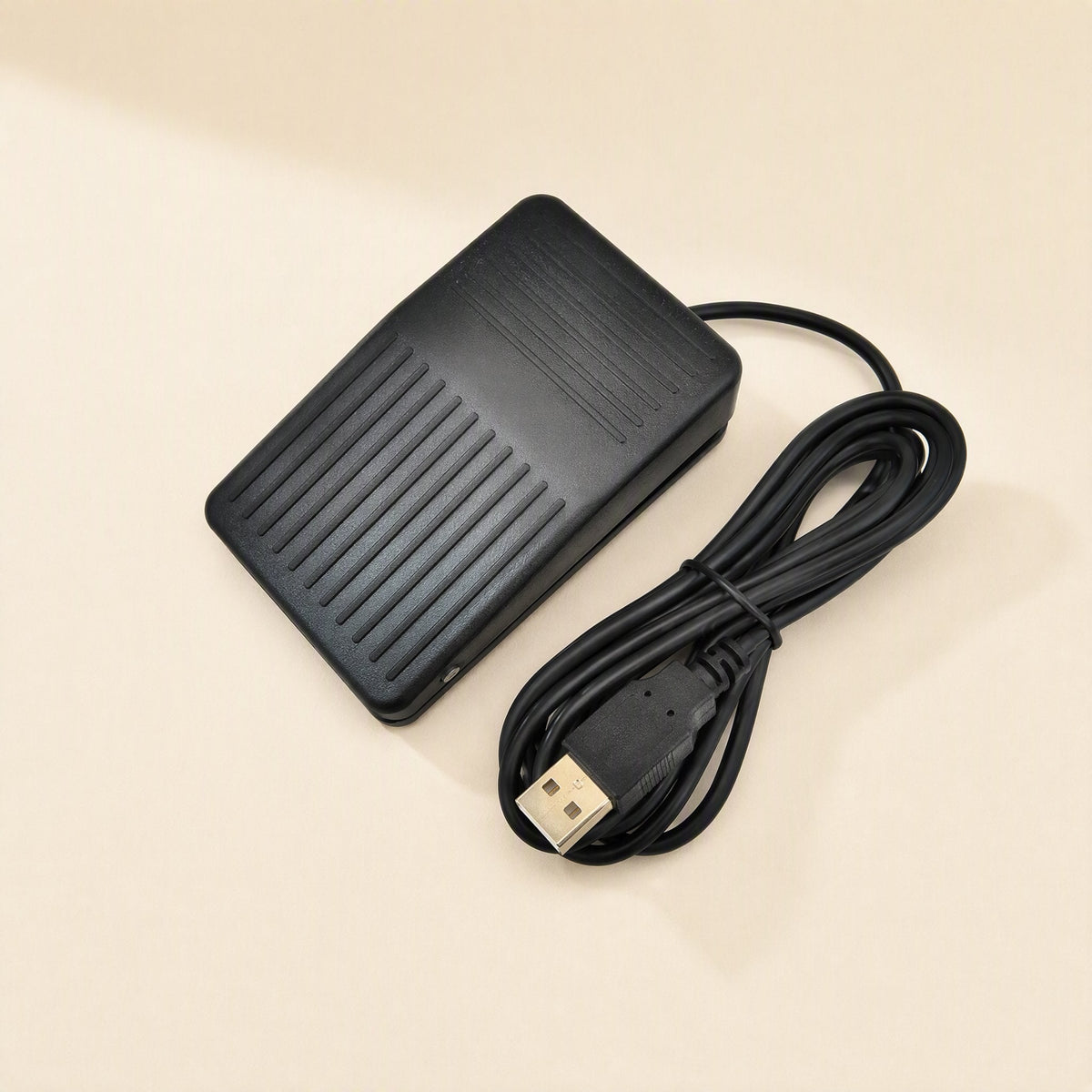 Tapstep – Black foot pedal with ridged top and coiled USB cable with gold-tipped plug, angled overhead view