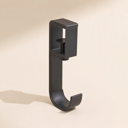 Softperch – Black screw-clamp headphone hook with a curved cradle, side view on a cream backdrop