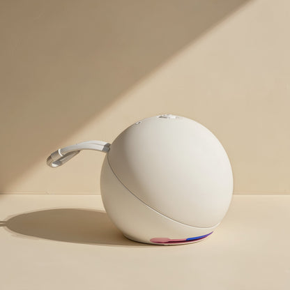 Roamnote – White spherical speaker with a pink and purple light accent and a white carry strap on a pale tabletop