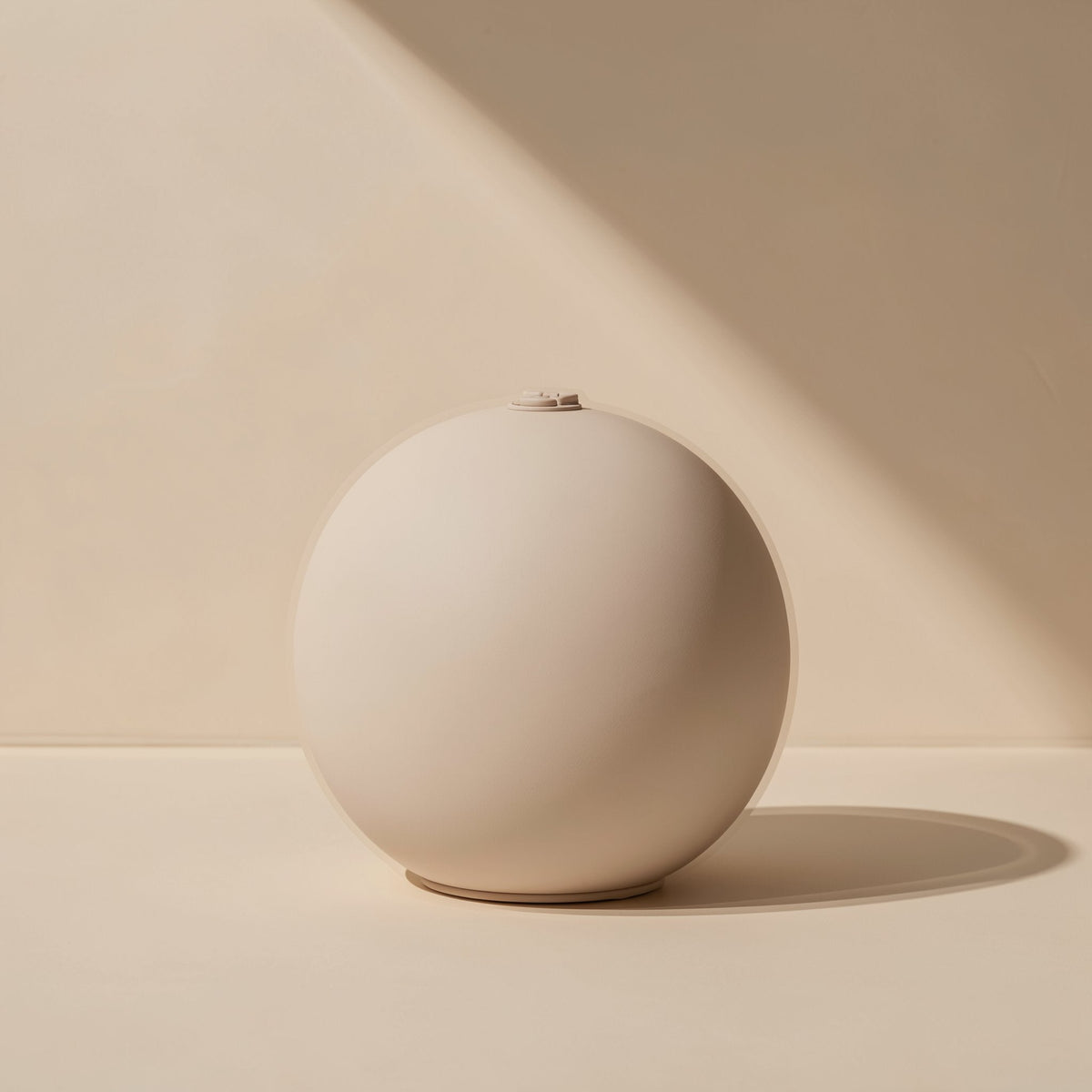 Roamnote – Cream-colored spherical speaker seen from the front, with a small button detail on top, against a beige wall