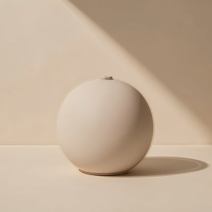 Roamnote – Cream-colored spherical speaker seen from the front, with a small button detail on top, against a beige wall