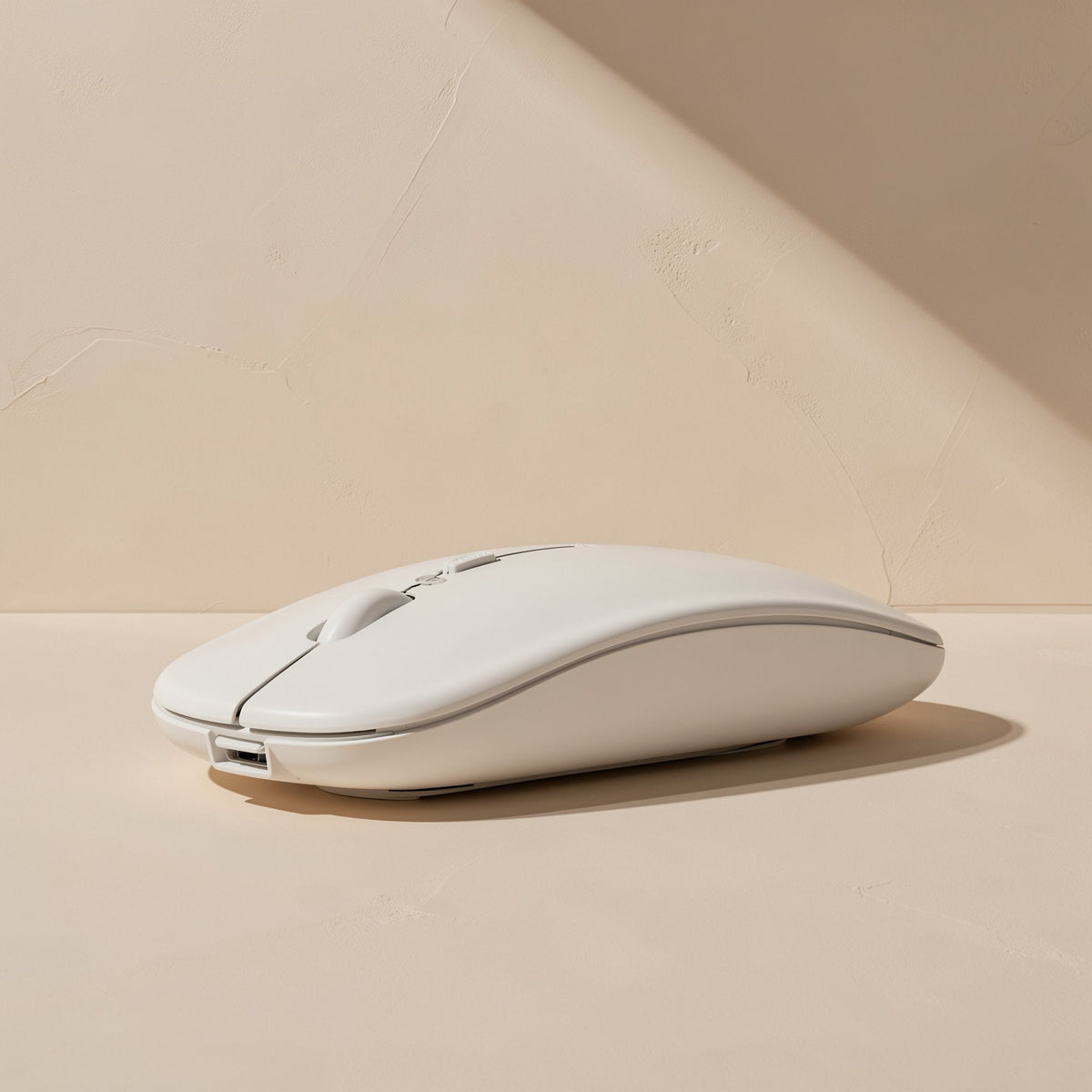 Roamclick – White wireless mouse seen from the front, showing the scroll wheel and USB charging port on a beige surface